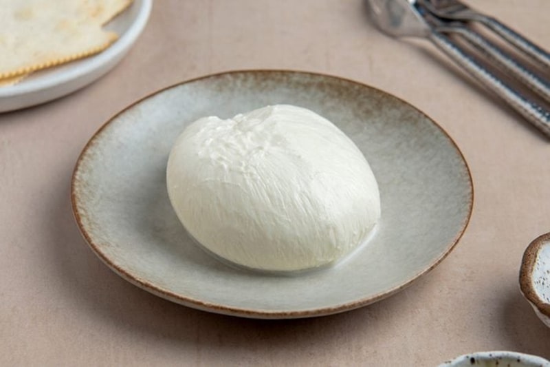 Burrata sau khi được gói và tạo hình hoàn chỉnh, với lớp vỏ Mozzarella mịn màng ôm trọn phần nhân béo mềm bên trong.